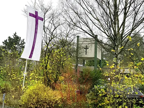 Blick zum Glockenturm, im Vordergrund eine Fahne mit lila Kreuz auf weißem Stoff.